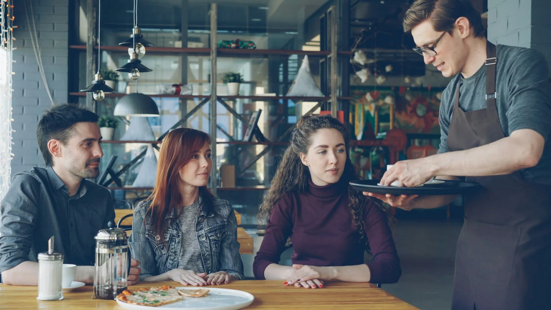 Mesero llevando una bandeja con el pedido a la mesa de sus clientes